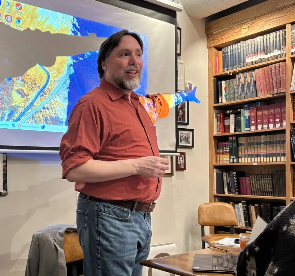 Rabbi Josh Breindel gesturing while teaching at Lehrhaus, with projected map and bookshelves behind him